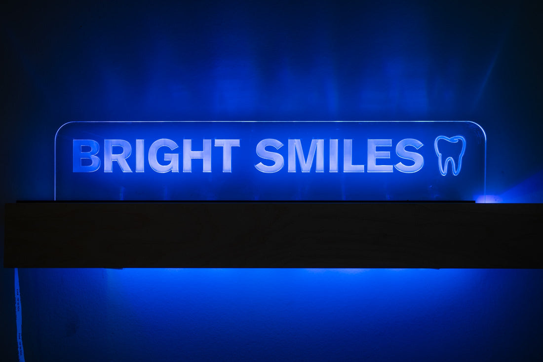 Edge-lit acrylic LED sign engraved with BRIGHT SMILES and a tooth logo, glowing blue on a dark base