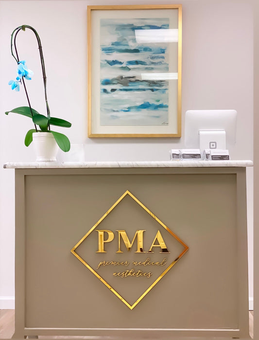 Mirrored gold acrylic PMA logo sign in a diamond frame mounted on the front of a taupe reception desk