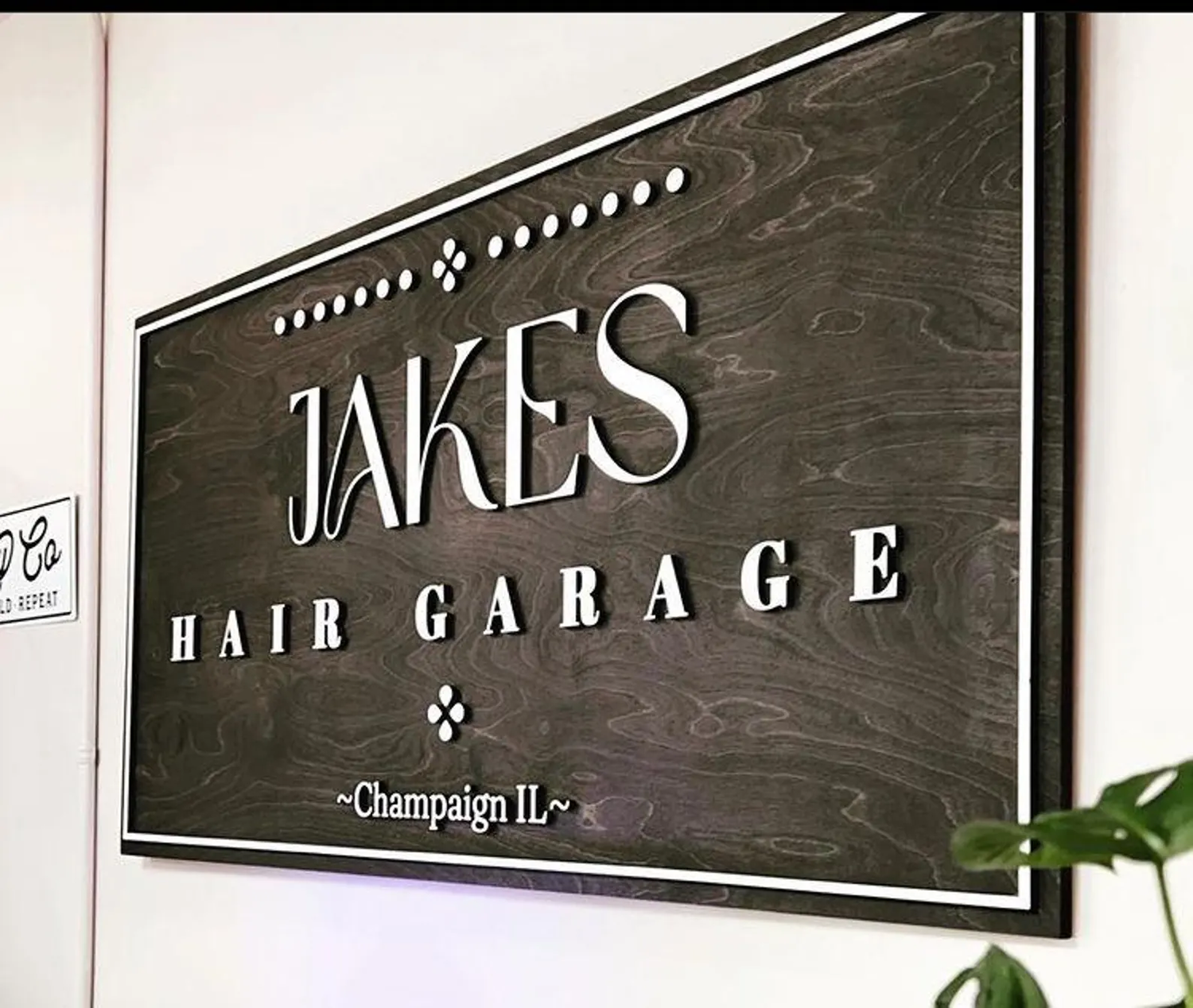 Wooden sign with 'Jakes Hair Garage' text on a white wall.