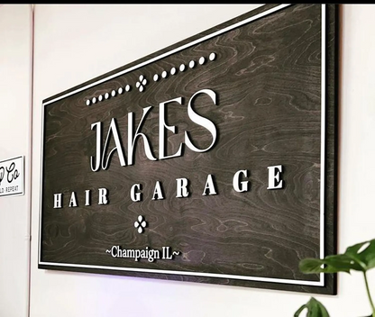 Wooden sign with 'Jakes Hair Garage' text on a white wall.